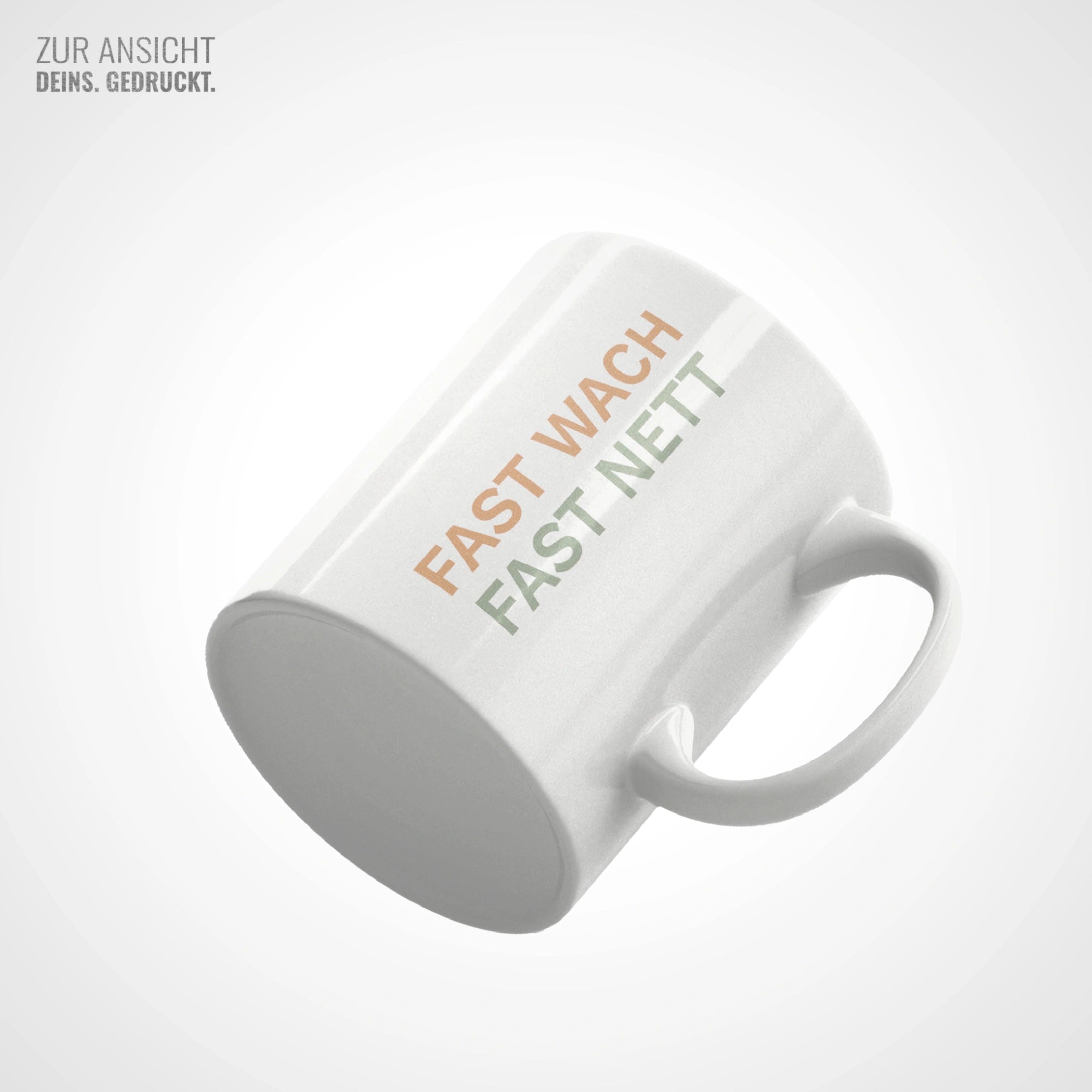 Weiße Keramiktasse mit Aufdruck "FAST WACH FAST NETT" in Orange und Salbeigrün, liegend fotografiert